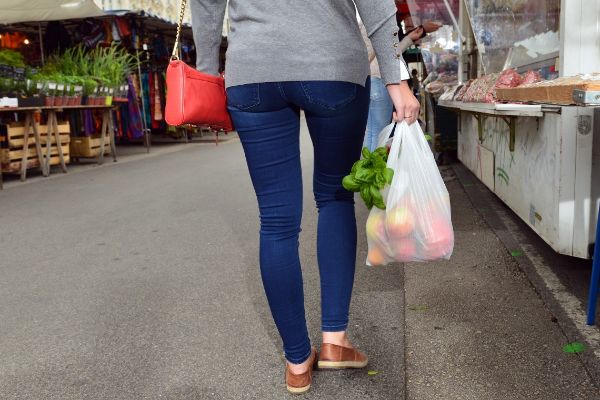 At the market, a woman carries a plastic bag of groceries.