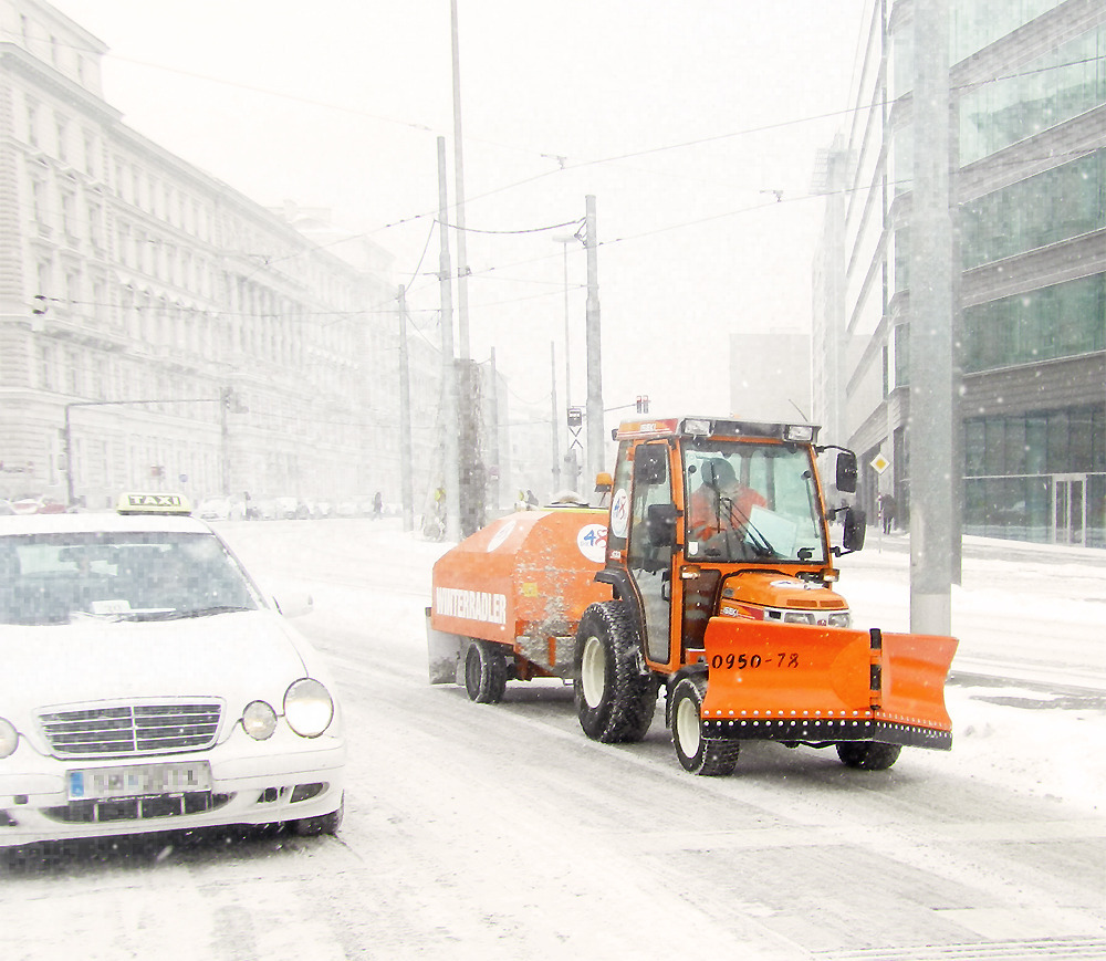 Auf der verschneiten Straße fährt ein Streu- und Räumfahrzeug